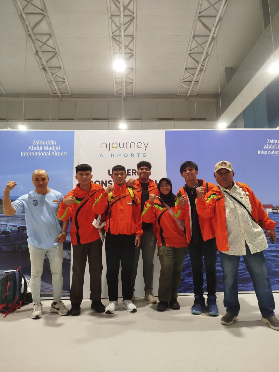 Foto: Tim PABSI NTB saat tiba di Bandara Internasional Zainuddin Abdul Madjid sebelum bertolak ke Bandung untuk mengikuti Kejurnas Angkat Besi Youth dan Junior 2025. Tampak Coach Suhaili (kiri) mengenakan kaos biru muda, dan Coach Sorie Enda Nasution (kanan) mengenakan topi serta jaket oranye.